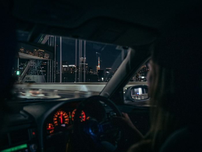 Inside a car at night, looking past the driver through the windshield at city lights