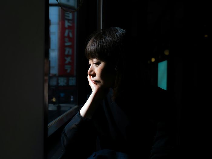 A woman rests her chin in her hand and looks out of a window, lost in thought